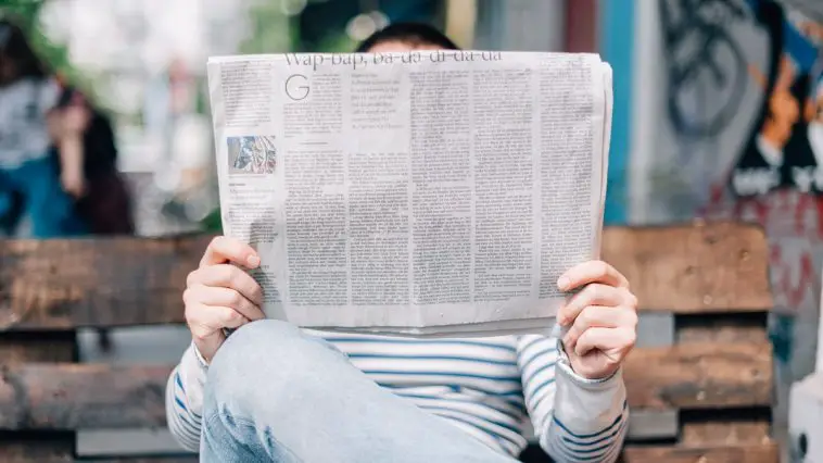 man sitting on bench reading newspaper