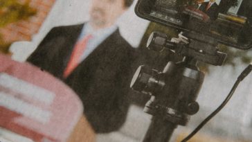 man in black suit jacket holding black camera